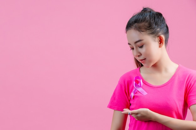 Conscientização do câncer de mama, mulher de camiseta rosa com fita de cetim rosa no peito, apoiando o símbolo