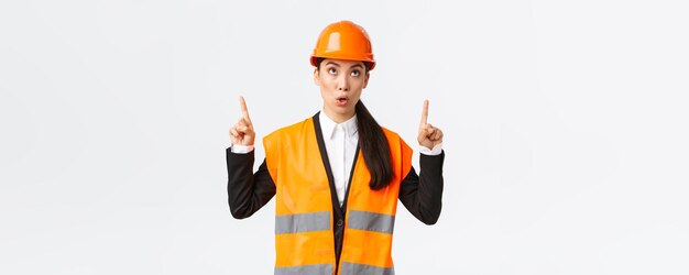 Construção civil e conceito industrial Engenheiro de gerente de construção feminino asiático surpreso e curioso em capacete de segurança e roupas reflexivas apontando os dedos para cima no banner interessante