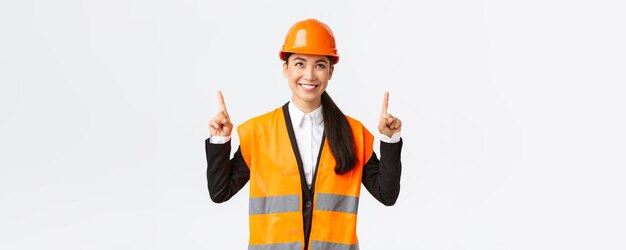 Construção civil e conceito industrial Vendedora asiática bem sucedida satisfeita mostrando aos clientes objeto para venda Engenheiro ou arquiteto apontando os dedos para cima usando capacete de segurança