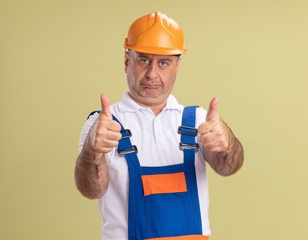 Construtor adulto confiante com o polegar para cima de duas mãos isoladas na parede verde