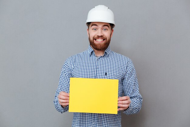 Construtor de homem barbudo alegre segurando papel em branco