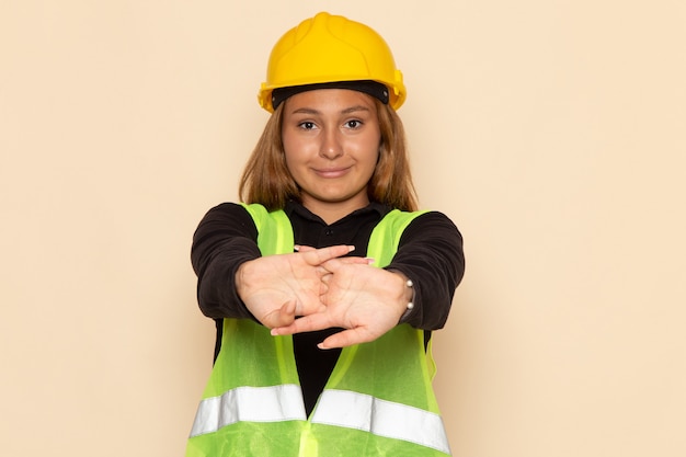 Construtor feminino de vista frontal com capacete amarelo sorrindo na parede branca feminina