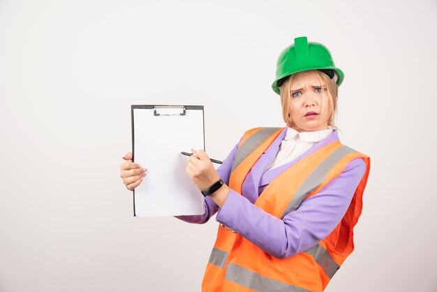 Construtor feminino no capacete de segurança segurando o tablet na parede branca.