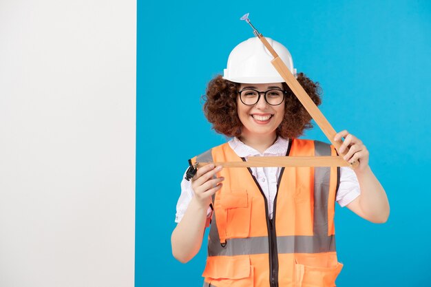 Construtor feminino sorridente de vista frontal de uniforme com ferramenta de madeira em azul