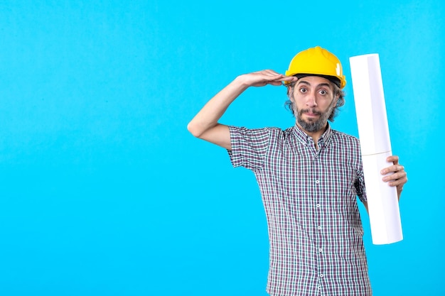 Construtor masculino de vista frontal com capacete amarelo com plano sobre fundo azul.