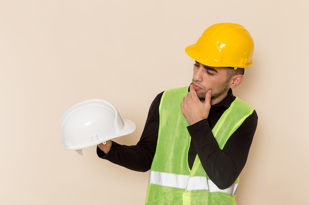 Construtor masculino de vista frontal com capacete amarelo segurando capacete branco sobre fundo claro