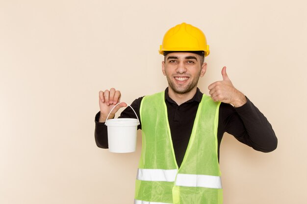 Construtor masculino de vista frontal com capacete amarelo segurando tinta sobre o fundo claro