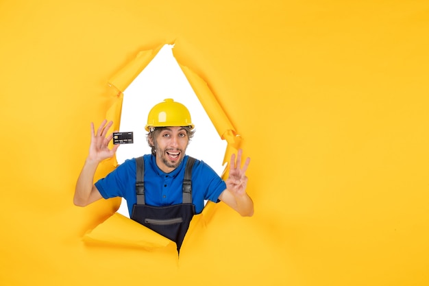 Construtor masculino de vista frontal de uniforme segurando um cartão do banco preto sobre fundo amarelo