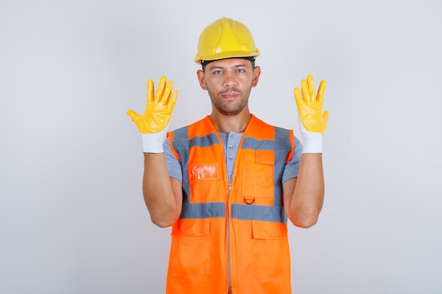 Construtor masculino em uniforme, levantando as mãos e mostrando os dedos, vista frontal.