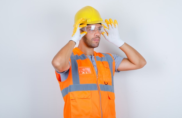 Construtor masculino usando óculos de segurança de uniforme, capacete, luvas, vista frontal.