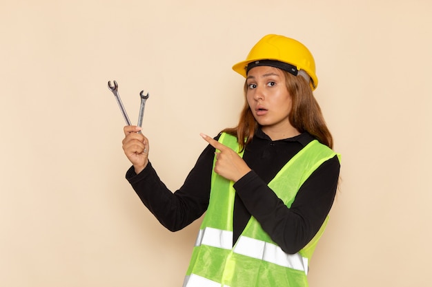 Construtora de frente com capacete amarelo segurando instrumentos de prata na parede de luz arquiteta