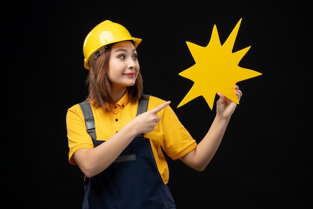 Construtora de frente, de uniforme, segurando uma figura amarela na parede preta