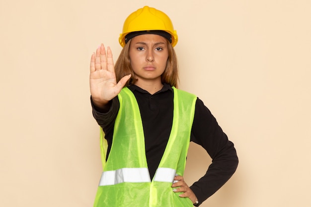 Construtora de frente feminina com capacete amarelo mostrando sinal de pare na parede branca feminina