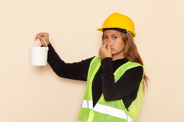 Construtora feminina com capacete amarelo e camisa preta segurando tinta fechando o nariz na mesa branca arquiteta construtora