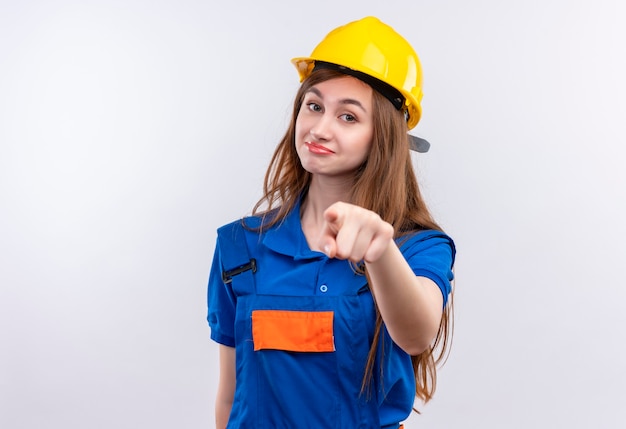 Construtora jovem com uniforme de construção e capacete de segurança, parecendo confiante apontando com o dedo indicador