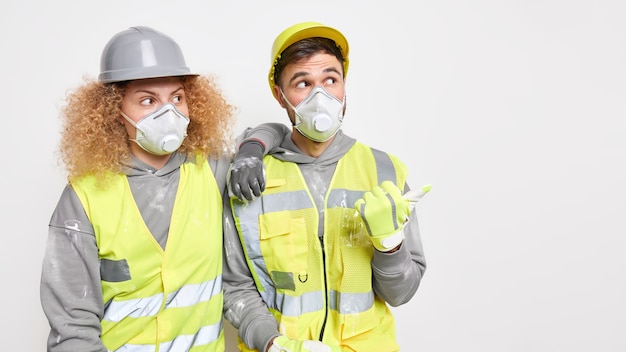 Construtores de capacetes de segurança, respiradores e roupas de trabalho ficam próximos um do outro.