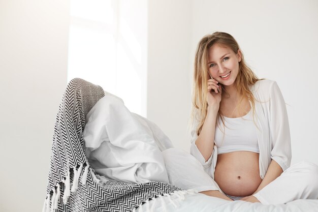 Consulta pré-natal. mulher falando no telefone com o ginecologista ou o médico do bebê, sorrindo, relaxando e curtindo sua casa de família