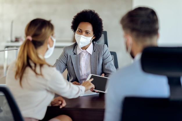 Foto grátis consultor financeiro afro-americano e seus clientes usando tablet digital enquanto usavam máscaras protetoras durante a reunião