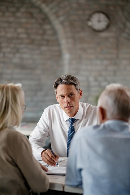 Consultor financeiro e casal sênior conversando enquanto analisa documentos durante consultas no escritório