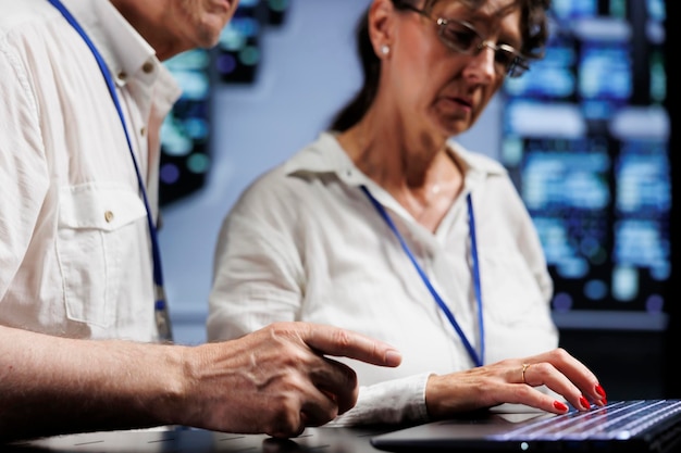 Foto grátis consultores de suporte técnico idosos trabalhando para manter o tempo de atividade em locais de alta tecnologia. especialistas qualificados debatendo soluções para racks de servidores de data centers travando, tentando consertar componentes