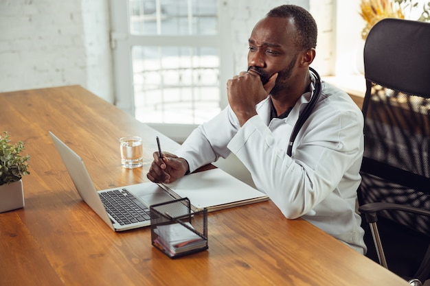 Consultoria médica para paciente, ouvindo médico afro-americano estressado durante seu trabalho com pacientes, explicando receitas de remédios. Trabalho árduo diário pela saúde e salvamento de vidas durante a epidemia.