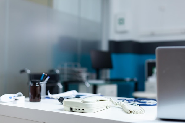 Consultório médico vazio moderno equipado com instrumentos médicos profissionais prontos para consulta clínica. Quarto de hospital sem ninguém com otoscópio e telefone fixo na mesa da mesa. Conceito de medicina