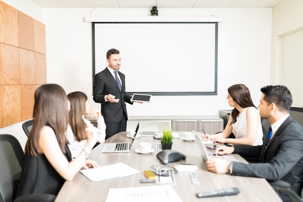 Contador masculino segurando tablet digital enquanto planeja orçamento com equipe na sala de reuniões