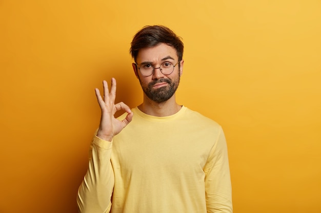 Conte comigo. Homem barbudo assertivo, de aparência séria, dá sinal de bom ou ótimo, dá aprovação, olha diretamente, garante resultado positivo, diz boa escolha, gosta de ideia, vestido casualmente