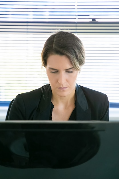 Foto grátis conteúdo feminino ceo sentado e trabalhando no computador. bem sucedida pensativa linda empresária fazendo seu trabalho, pensando e olhando para baixo no monitor. conceito de negócio, expressão e fluxo de trabalho