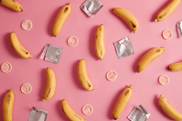 Foto grátis contracepção, conceito erótico. bananas amarelas e preservativos desembrulhados por aí. conscientização da aids. composição plana lay. relacionamentos seguros. fundo rosa. proteja-se. prevenção de doenças venéreas