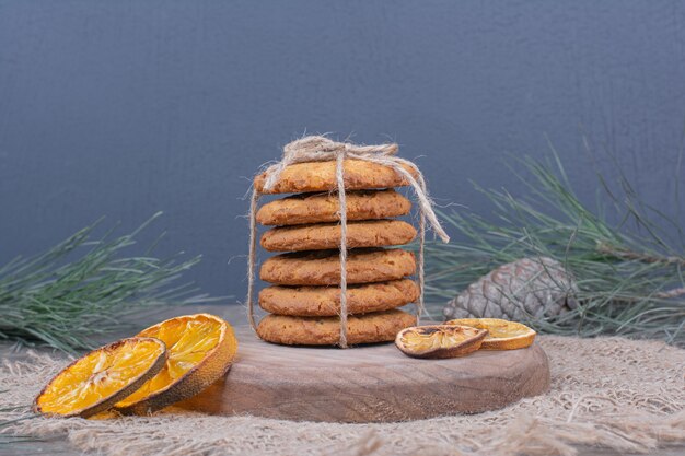 Cookies amarrados com um fio em uma placa de madeira com rodelas de laranja secas