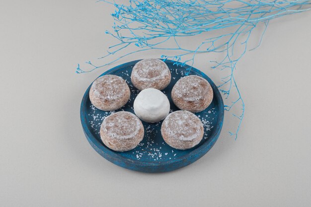 Cookies com revestimento em pó de baunilha em uma pequena bandeja ao lado de galhos azuis sobre fundo de mármore.