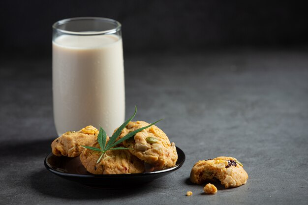 Cookies de cannabis e folha de cannabis colocados em uma tigela preta servida com um copo de leite