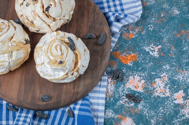 Cookies de merengue branco com passas pretas em uma placa de madeira.