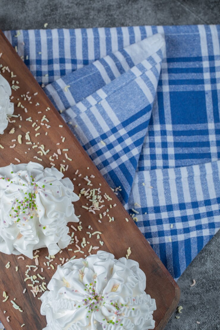 Foto grátis cookies de merengue branco com pó de coco em uma placa de madeira na toalha azul.