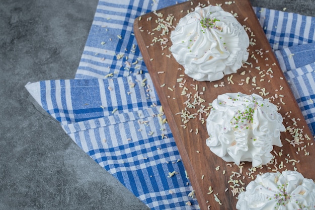 Cookies de merengue branco em uma placa de madeira com pó de coco na parte superior.