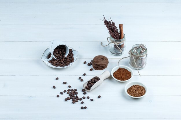 Cookies de vista de alto ângulo, xícara de grãos de café com uma tigela de café instantâneo, pote de ervas no fundo branco da placa de madeira. horizontal