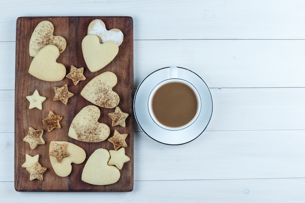 Foto grátis cookies em forma de coração e estrela plana leigos na tábua de madeira com uma xícara de café no fundo branco da placa de madeira. horizontal