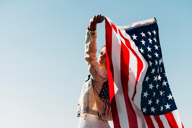 Cool jovem mulher segurando bandeira americana, olhando por cima do ombro