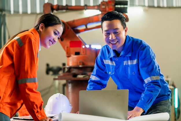 Cooperação do engenheiro Dois técnicos asiáticos masculinos e femininos de manutenção inspecionam o sistema de robô de relé com tablet laptop para controlar a qualidade operar o processo de trabalho indústria pesada 40 fábrica de fabricação