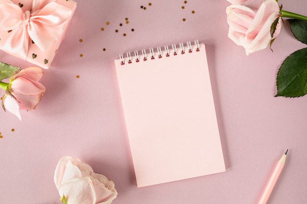 Copie o bloco de notas de espaço para o seu texto sobre um fundo rosa claro com rosas cor de rosa e caixas de presente. colocação plana. Vista do topo.