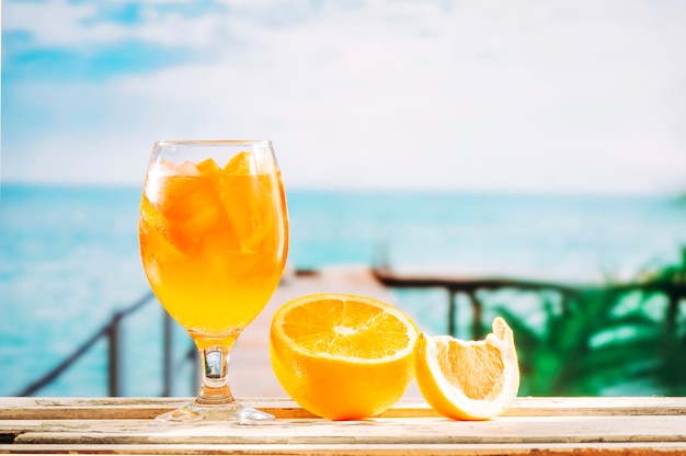 Copo com bebida de laranja e laranja fatiada na mesa de madeira