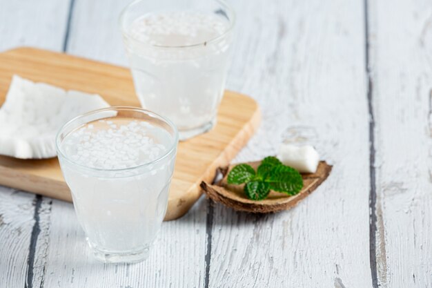 Copo de água de coco colocado sobre fundo branco de madeira