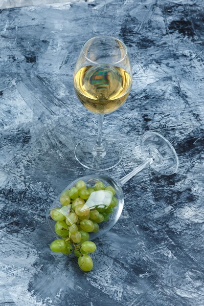 Copo de close-up de uvas brancas com copo de uísque em fundo de mármore azul escuro. vertical