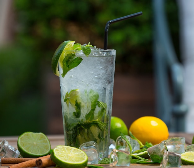 Copo de coquetel de mojito com pedaços de gelo, folhas de hortelã fresca e fatias de limão com tubo