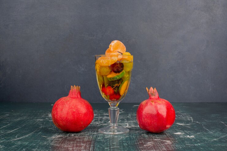Foto grátis copo de frutas e romãs na mesa de mármore.