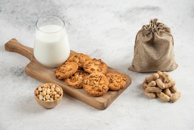 Copo de leite e biscoitos na tábua de madeira com amendoim.