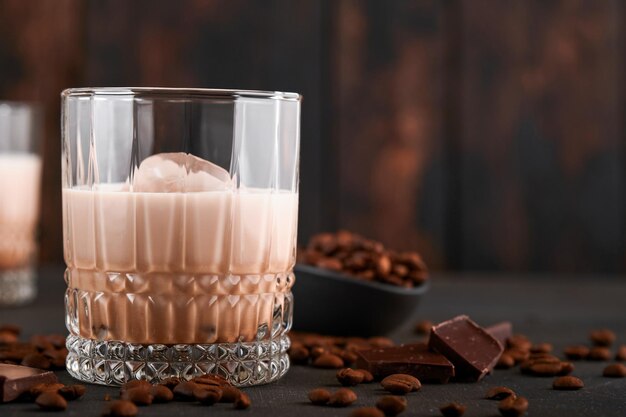 Copo de licor de baileys creme irlandês com grãos de café torrados, canela e chocolate na mesa de fundo de madeira escura. foco seletivo.