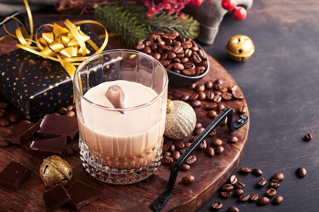 Copo de licor de baileys de creme irlandês com gelo, grãos de café torrados, canela, decoração de natal e chocolate na mesa de fundo de madeira escura. mesa de natal com presentes. foco seletivo.