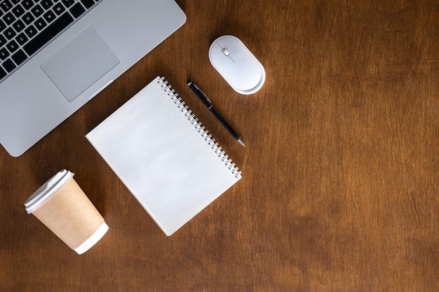 Copo de papel de notepad de laptop e mouse de computador em uma vista de mesa de madeira